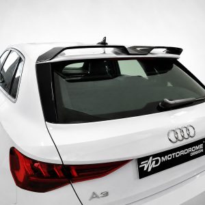 White Audi A3 rear-left view with a roof spoiler and red taillights in a showroom setting.