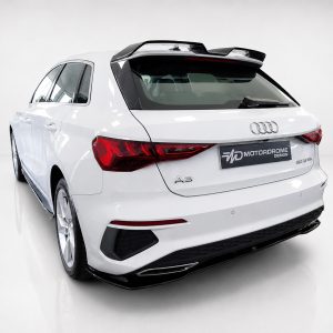White Audi A3 hatchback photographed from the rear-left in a bright studio, showing the taillights and roof spoiler.