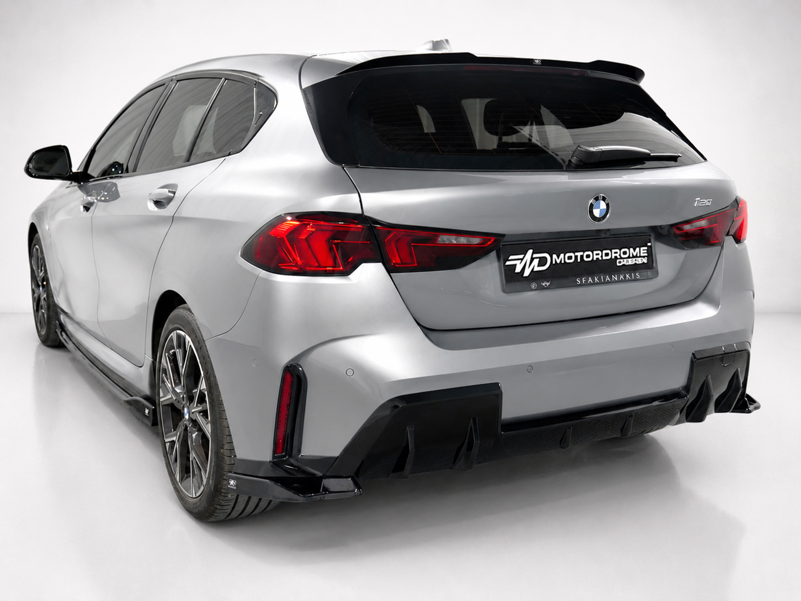 A-546_2jpg - OPSHOLDERS Rear three-quarter view of a silver BMW SUV with a black rear diffuser and prominent red taillights, displaying a MOTOR DROME license plate.