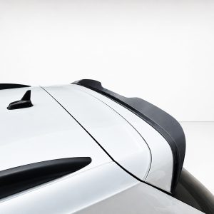 Close-up of a white car roof showing a black roof rail, antenna, and rear spoiler against a light background