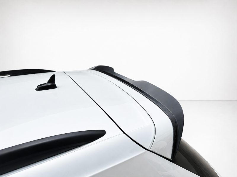 Close-up of a white car roof showing a black roof rail, antenna, and rear spoiler against a light background