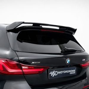Rear view of a black BMW SUV showing a performance spoiler, taillights, and badging (XDrive and M) with a Motordrome Design plate on the bumper.