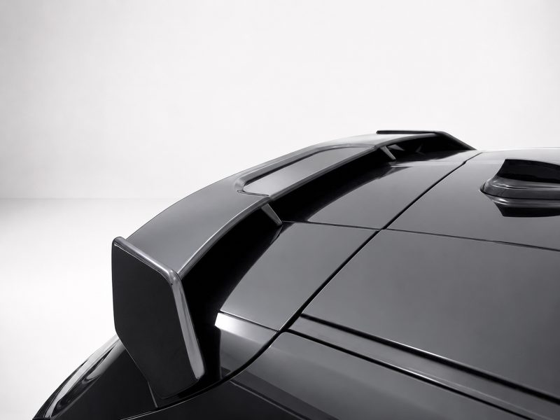 Close-up of a glossy black car roof with a rear spoiler against a light background, highlighting its aerodynamics.
