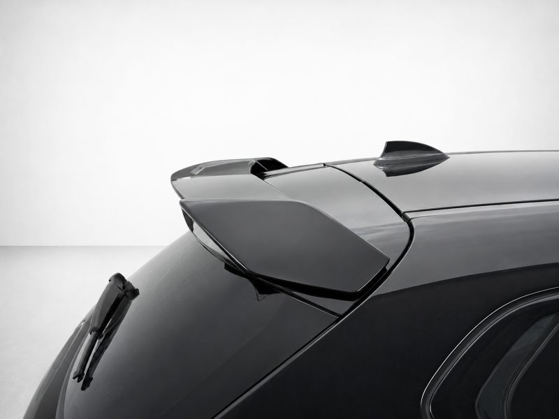 Close-up of a glossy dark car roof with a rear spoiler and shark-fin antenna, showing smooth reflections.