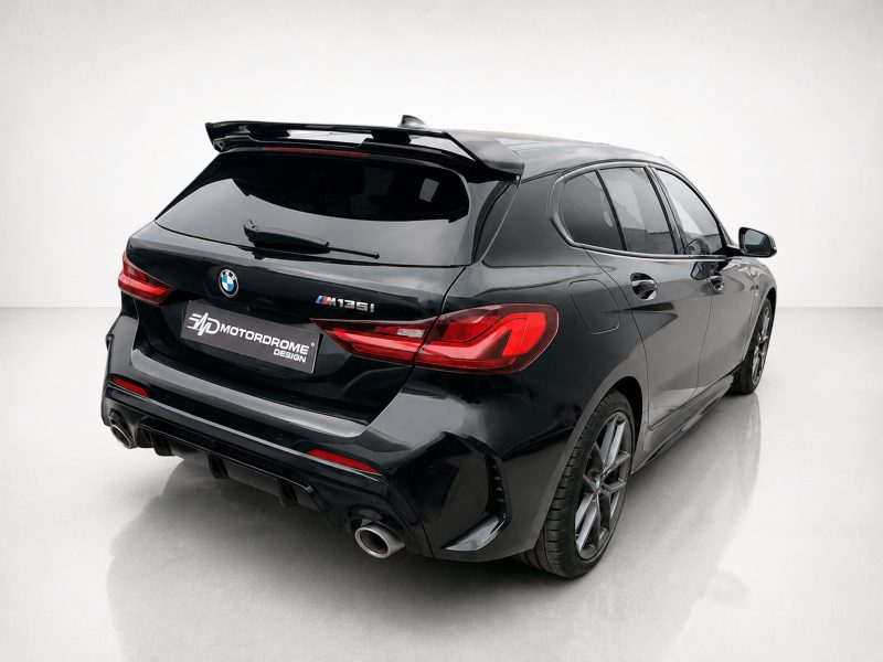 Rear three-quarter view of a black BMW M135i with large spoiler and aggressive rear diffuser in a studio setting, showing red taillights and dual exhausts.