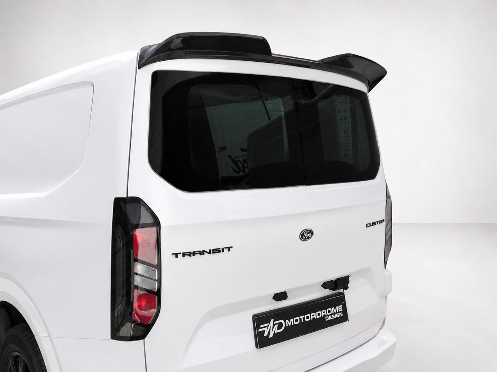 A-550_1jpg - OPSHOLDERS Rear view of a white Ford Transit van with a dark rear window and roof spoiler on a neutral backdrop.