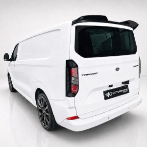 A-550_2jpg - OPSHOLDERS Rear three-quarter view of a white Ford Transit van with dark-tinted rear window and aftermarket black wheels; a custom logo plate reads 'MOTOR DROME DESIGN'.