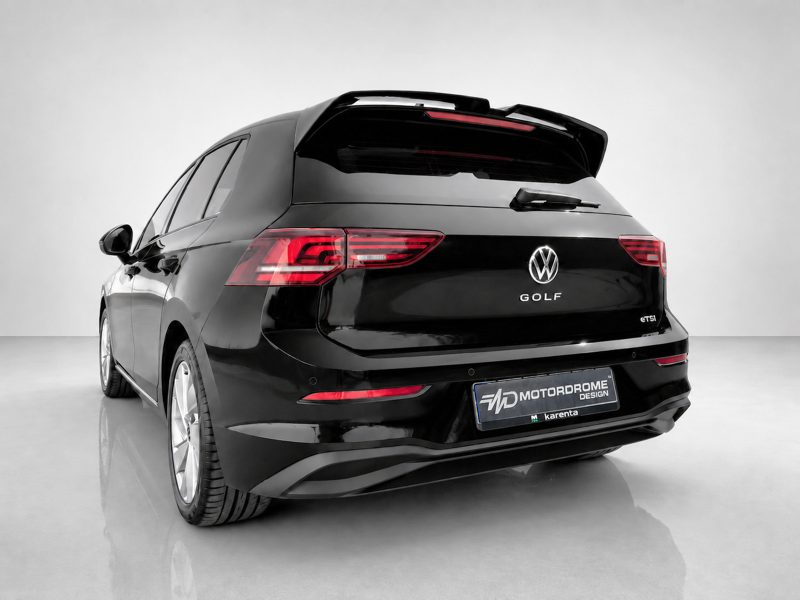 Rear view of a black Volkswagen Golf SUV with a roof spoiler in a bright studio setting, showing taillights and VW logo.",