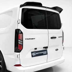 White Ford Transit Custom van rear view with black-tinted windows, rear spoiler, and MOTORDROME DESIGN plate visible on tailgate badges: TRANSIT and CUSTOM.