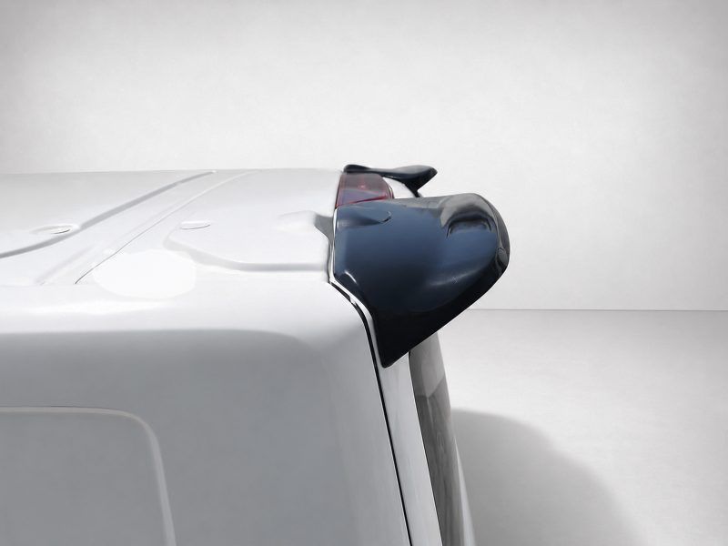 White vehicle seen from the rear side with a black rear spoiler on the roofline, against a neutral background.