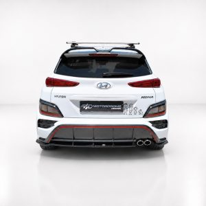 Rear view of a white Hyundai Kona with a roof rack and red-accented bumper diffuser, featuring a Motordrome Design plate and small cartoon decals on the bumper area.