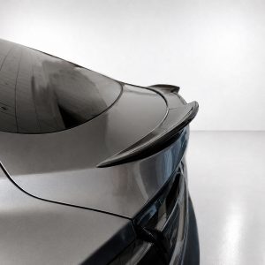 Rear view of a sleek silver car showing a prominent spoiler and curved trunk line in a glossy showroom setting.
