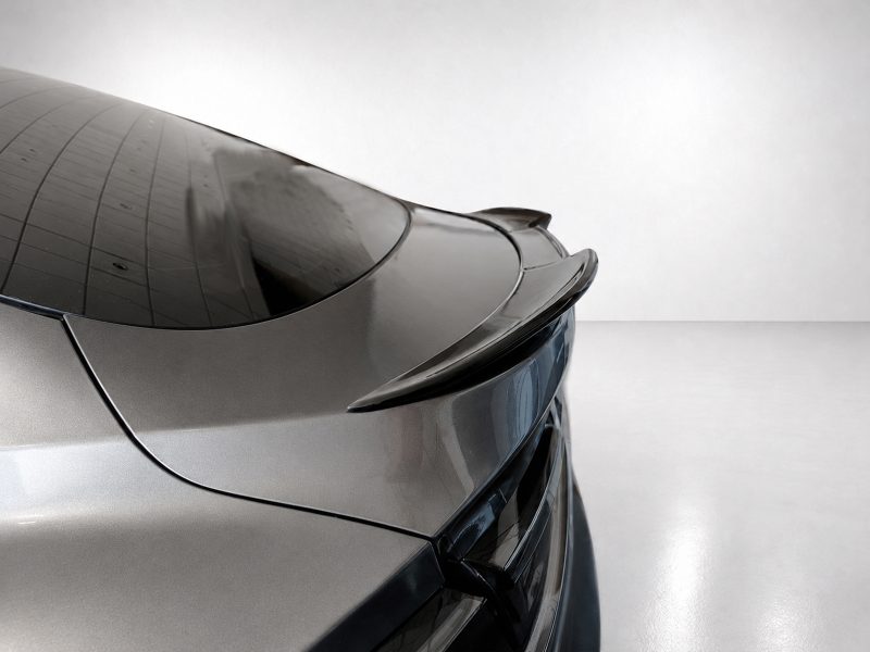 Rear view of a sleek silver car showing a prominent spoiler and curved trunk line in a glossy showroom setting.