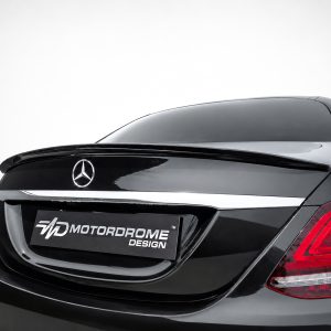 Rear view of a black Mercedes with a chrome trunk badge and red taillights, displaying a Motordrome Design plate.