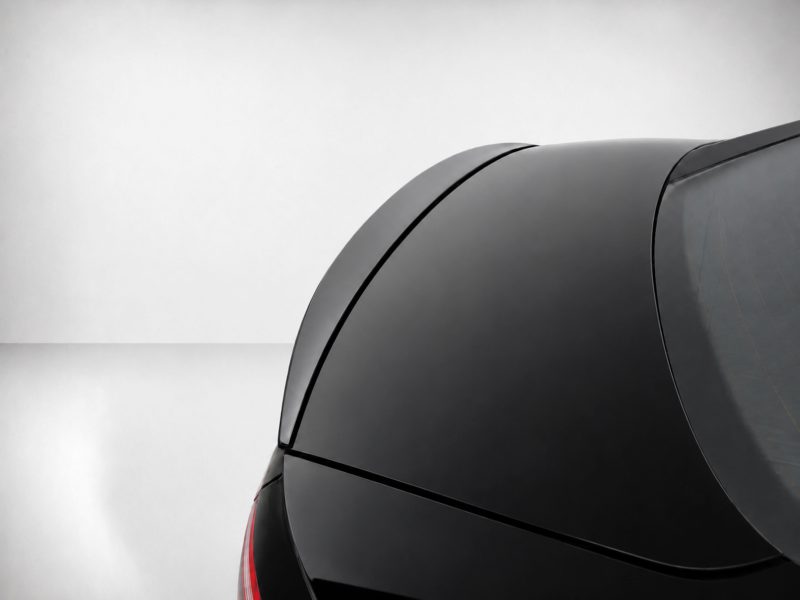 A-556_4jpg - OPSHOLDERS Close-up of the rear section of a glossy black car, featuring curved trunk lines and a red taillight on the left edge