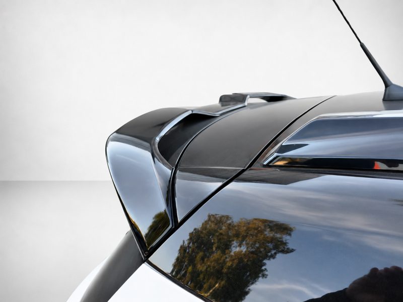 Close-up of the roof and rear area of a glossy dark car, featuring a raised spoiler and an antenna on the roofline.