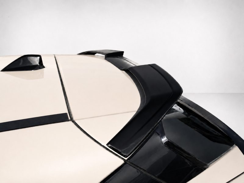 Close-up of a cream-colored car hood with black aerodynamic vents and trim, photographed from a low angle against a pale background.