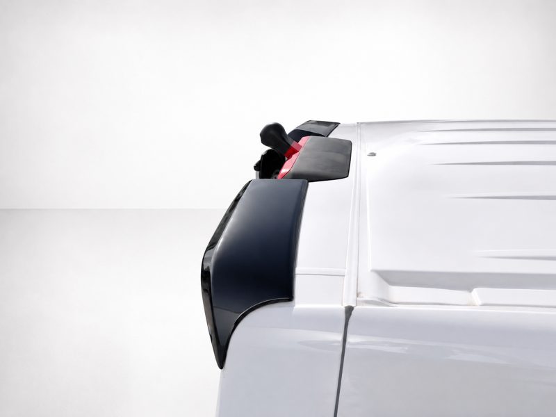 A-563_5jpg - OPSHOLDERS Close-up of a white truck cab's front corner, showing the black side mirror housing and door handle.