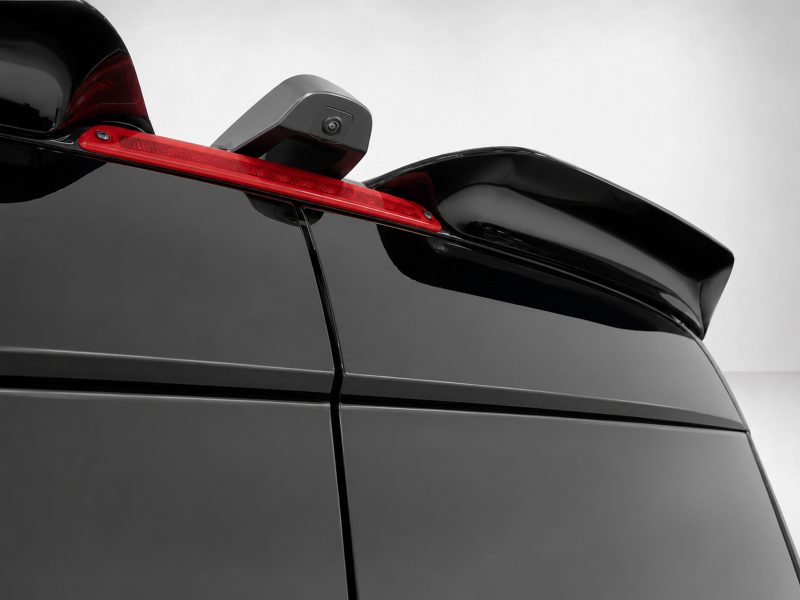 Close-up of a glossy black car rear with a red third brake light and a mounted camera on the spoiler.