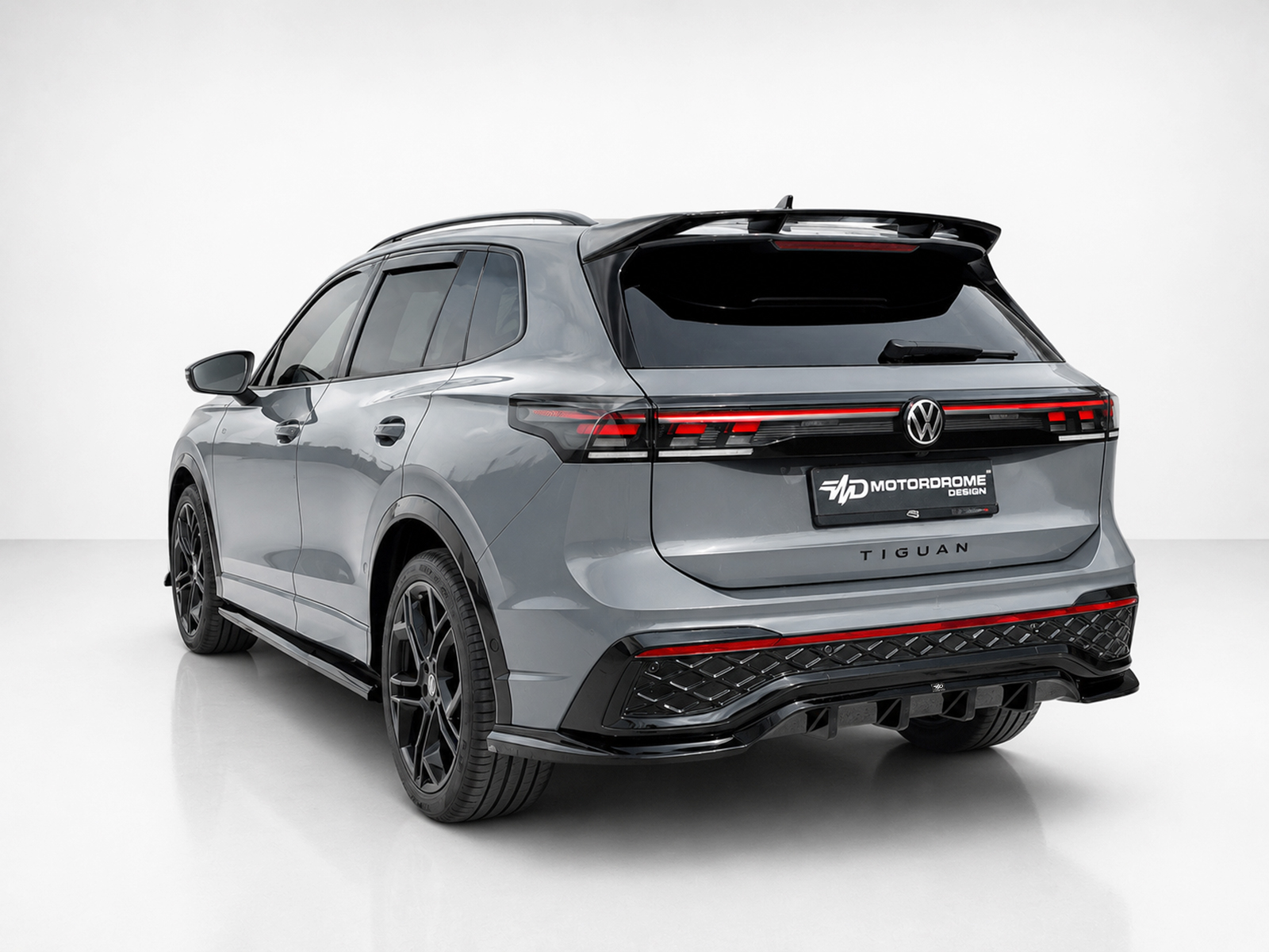 A-565_2jpg - OPSHOLDERS Rear three-quarter view of a gray Volkswagen Tiguan SUV in a studio setting with black alloy wheels and roof railsedicailed by a white backdrop.