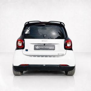 Rear view of a white Smart car with a black roof, taillights lit, and a center badge reading 'smart'.