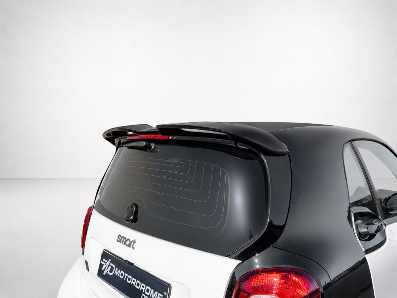 Rear view of a two-tone hatchback showing a rear spoiler, wiper, and curved red taillights against a light studio backdrop.