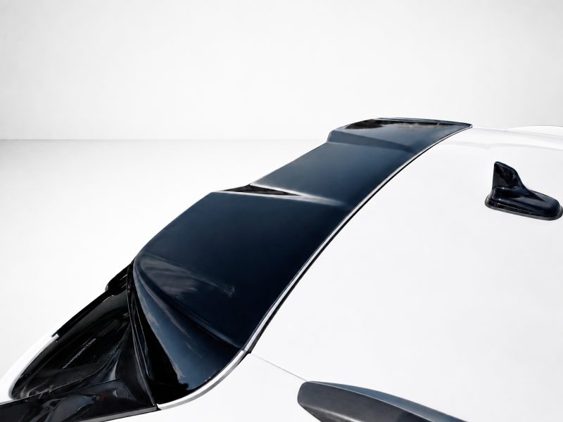 Aerial view of a white car showing a glossy black roof panel and windshield from above in a minimalist setting