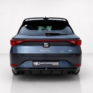 Rear view of a blue SEAT Leon FR hatchback with distinctive taillights and quad exhausts in a studio setting, showing the badge and design cues (MotorDrome plate visible).