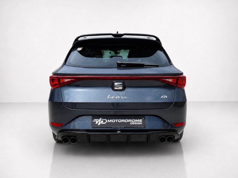 Rear view of a blue SEAT Leon FR hatchback with distinctive taillights and quad exhausts in a studio setting, showing the badge and design cues (MotorDrome plate visible).
