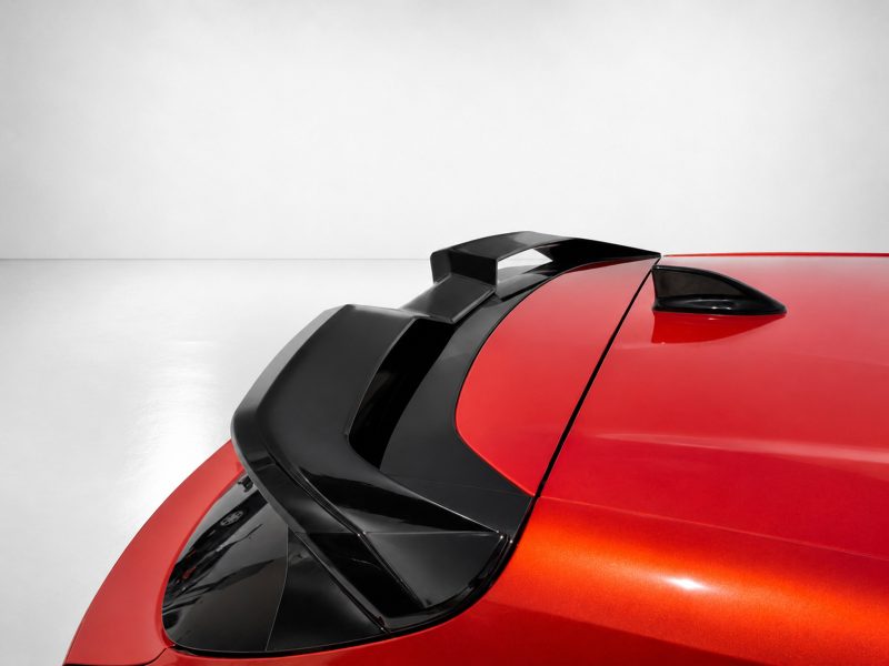 Close-up of a red sports car showing a black aerodynamic spoiler and roof details against a light gray background, emphasizing design lines.