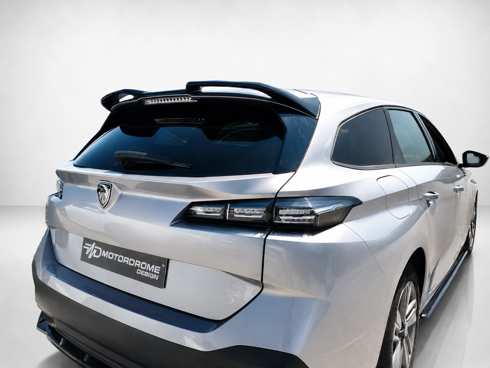 A-574_1jpg - OPSHOLDERS Rear view of a silver SUV with a roof spoiler, tinted rear window, and a MotorDrome Design badge.