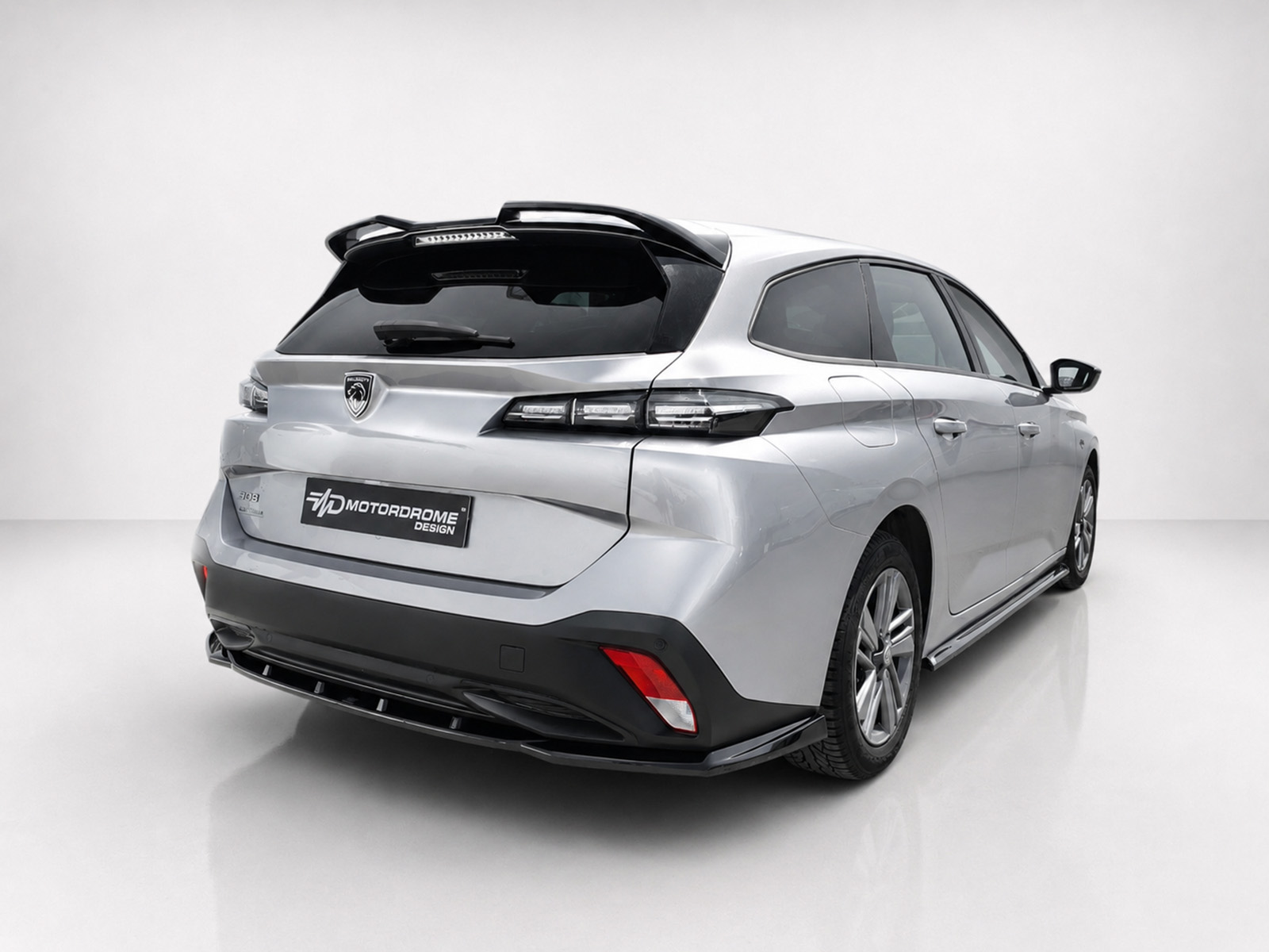 A-574_2jpg - OPSHOLDERS Rear three-quarter view of a silver SUV in a studio, highlighting the tail lights, roof spoiler, and a black rear license plate reading 'MOTORDROME DESIGN'.