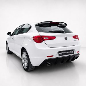 Rear view of a white Alfa Romeo Giulietta hatchback in a studio, showcasing red tail lights and a black rear diffuser.