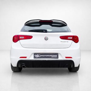 Rear view of a white Alfa Romeo Giulietta in a studio, showing tail lights, hatch, and a Motordrome Design plate above the bumper.
