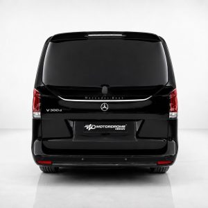A-578_3jpg - OPSHOLDERS Rear view of a glossy black Mercedes-Benz V300d van in a studio setting, with Mercedes logo and V300d badge visible underlit tailgate light strip.