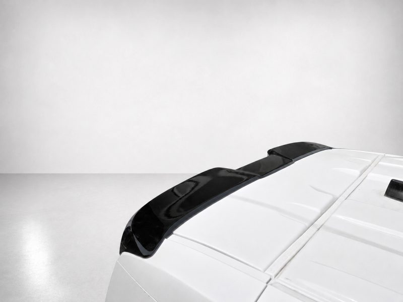 Rear portion of a white car with a black roof spoiler against a gray backdrop.
