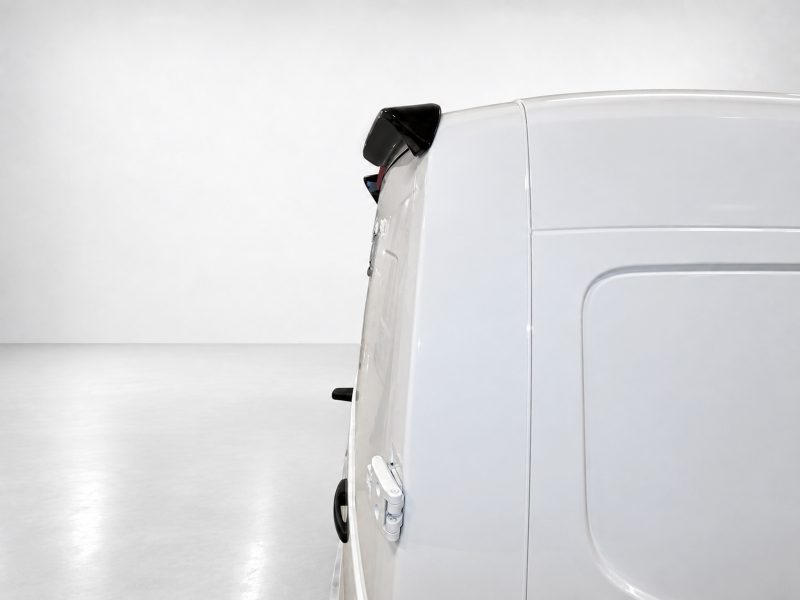Side view of a white cargo van with a visible rear door and taillight in a bright studio setting.