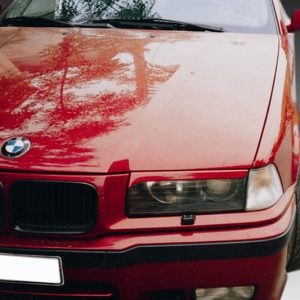 Close-up of a red BMW car's front end, showing the grille, headlight, and hood with reflections