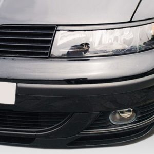 Close-up of the front end of a gray car, showing the headlight, grille, and lower bumper with a fog light on the right side.