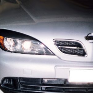 Close-up of a silver car's front end showing the left headlight, grille, and bumper area with a blurred background gradient to the left.