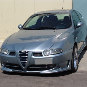 Front three-quarter view of a silver Alfa Romeo sedan parked on a concrete lot, showing the distinctive grille and rounded headlights.