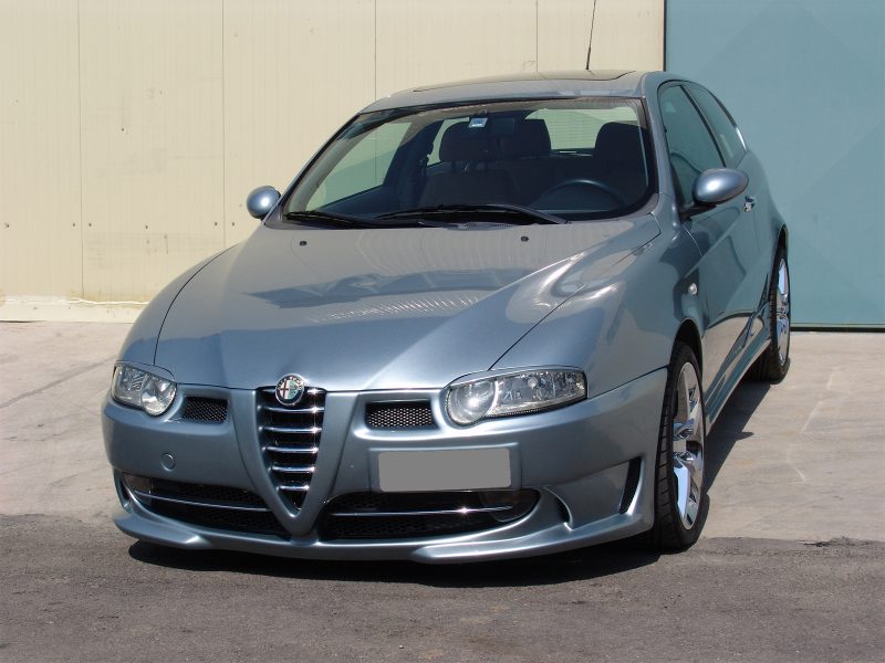 Front three-quarter view of a silver Alfa Romeo sedan parked on a concrete lot, showing the distinctive grille and rounded headlights.
