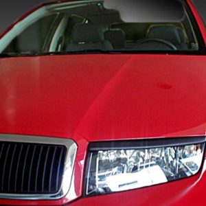 Front view of a red Skoda car, showing grille with emblem and headlight on the right side of the image.