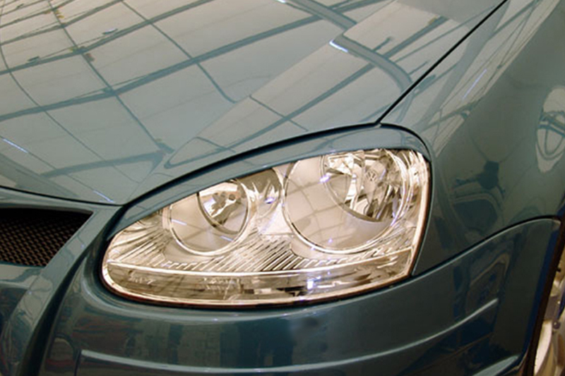 FR000088_1jpg - OPSHOLDERS Close-up of a teal car's front headlight on the left side, with reflections on the hood.