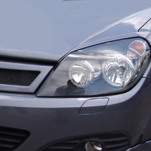 Close-up of the front left side of a dark gray car, showing the headlight, bumper, and grille.