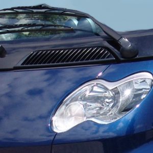 Close-up of a blue car's front end showing a headlight, hood vent, and windshield wipers.