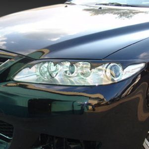 Front-left view of a black Mazda sedan, showing the headlight cluster, grille, and alloy wheel.
