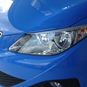 Blue car front close-up showing headlight, grille, and lower bumper detail.
