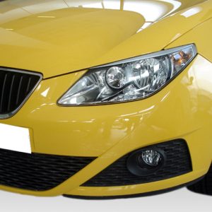 Front view of a bright yellow car showing the headlight, grille, and bumper, angled from the side.