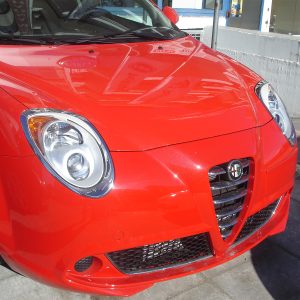Front view of a bright red Alfa Romeo car, showing its round headlights and distinctive grille outdoors.
